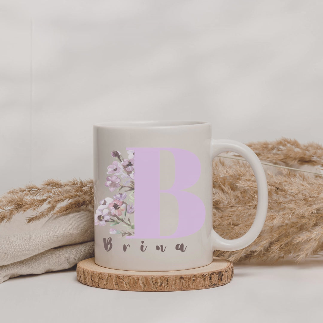 Weiße Tasse mit einem Blumen Motiv, einem Anfangsbuchstaben und einem Namen.