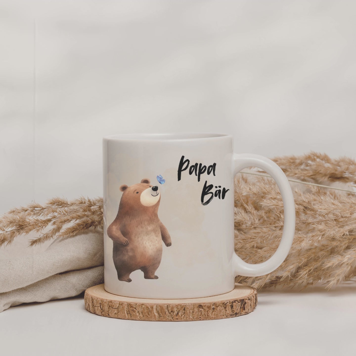 Weiße Tasse mit der Aufschrift "Papa Bär" und ein Motiv mit einem Bären drauf vor dem ein blauer Schmetterling fliegt
